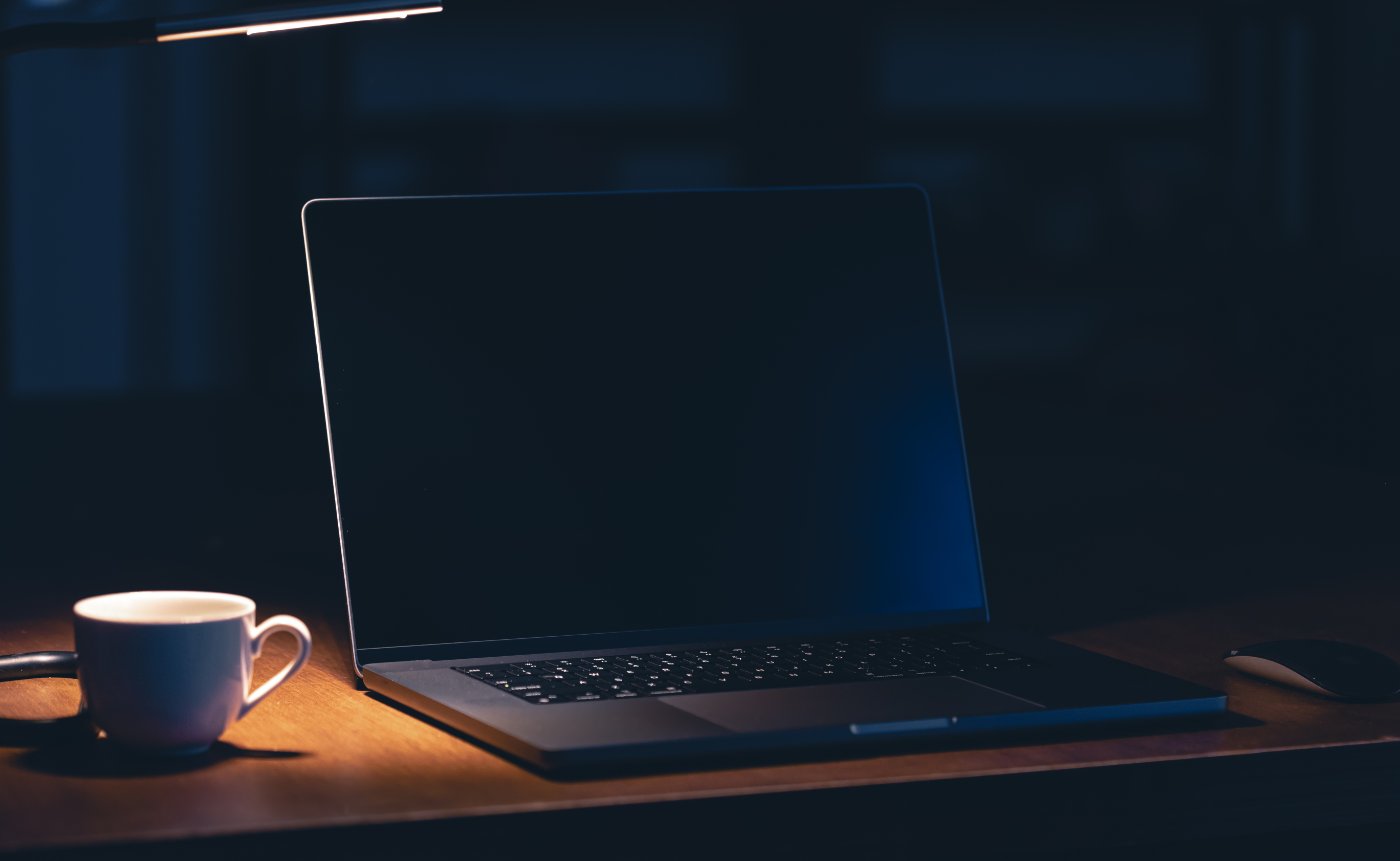 Arbeitsplatz mit Laptop und Kaffeetasse in einem dunklen Raum bei Nacht